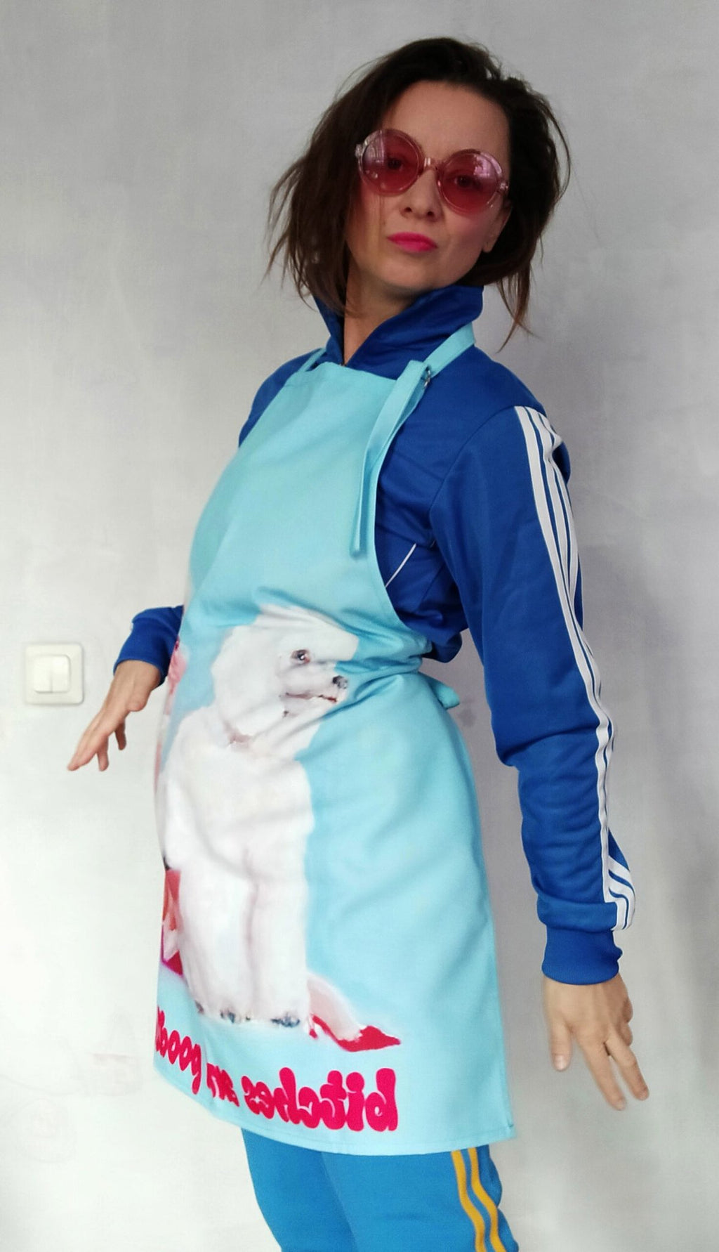 1. Woman wearing Katrin Valgemäe apron with poodle artwork, dressed in blue tracksuit and pink sunglasses
