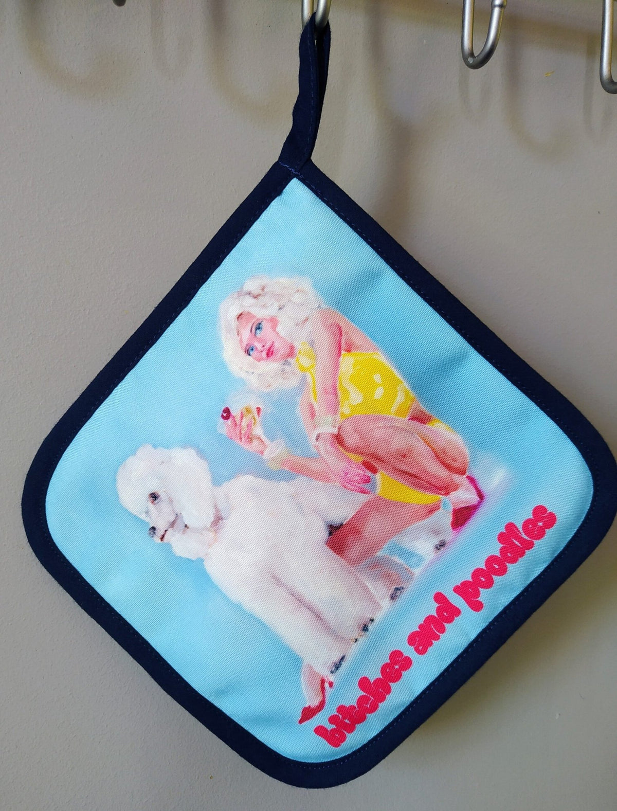 1. Hanging pot holder with pop art design of woman in yellow dress and poodle, text 'bitches and poodles' in red