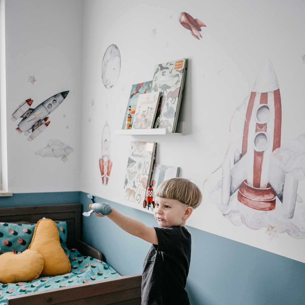 5. Child playing in a space-themed room with watercolor rocket wall stickers and books on shelves