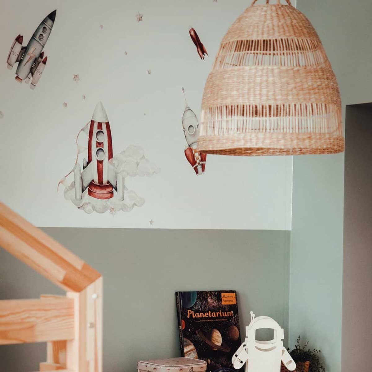 3. Space-themed room with watercolor rocket wall stickers and wicker lamp, featuring books and decor