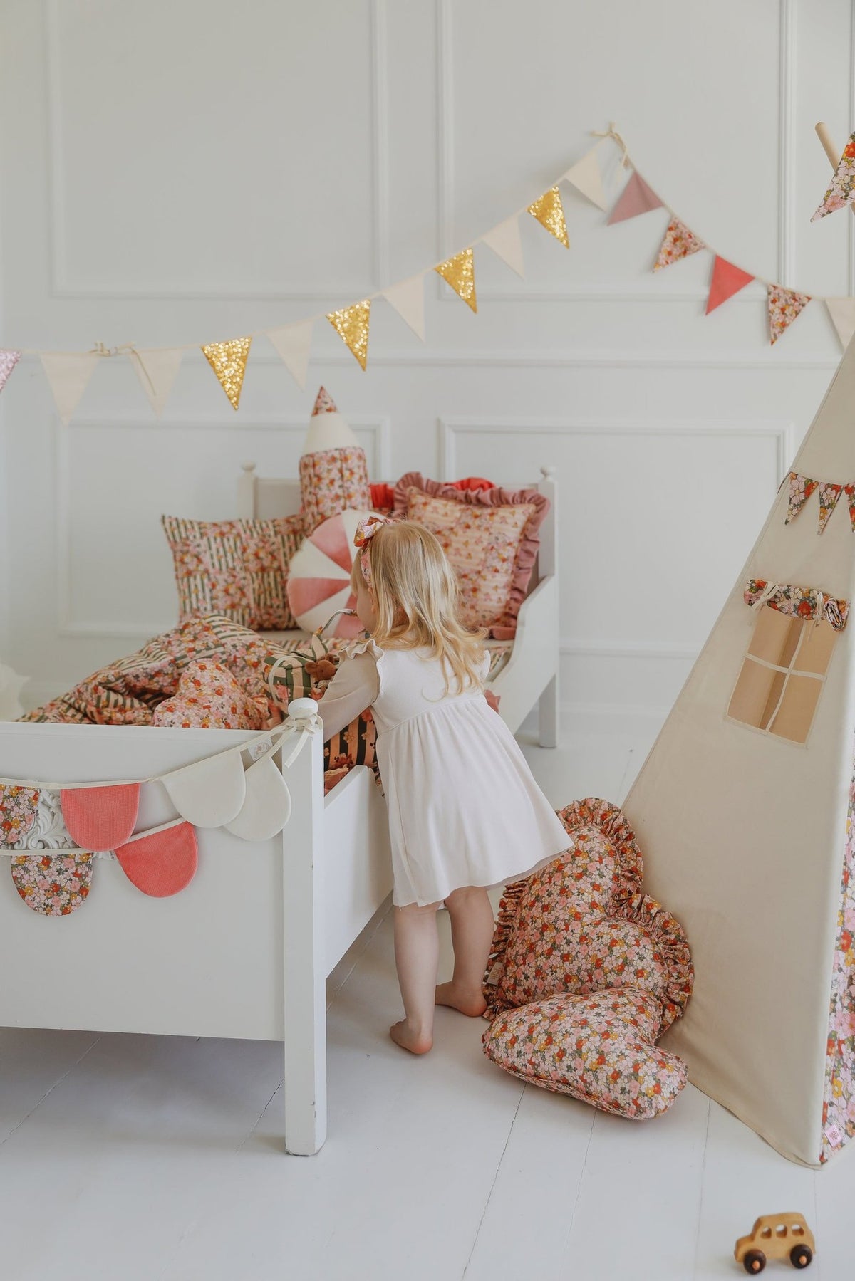 7. Little girl in a white dress in a decorated room with garland, teepee, and floral bedding