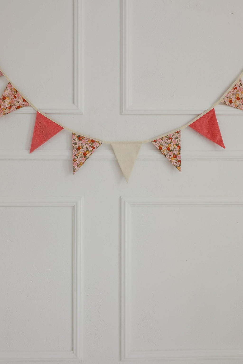 6. Close-up of garland with pink, floral, and beige pendants on a white paneled wall