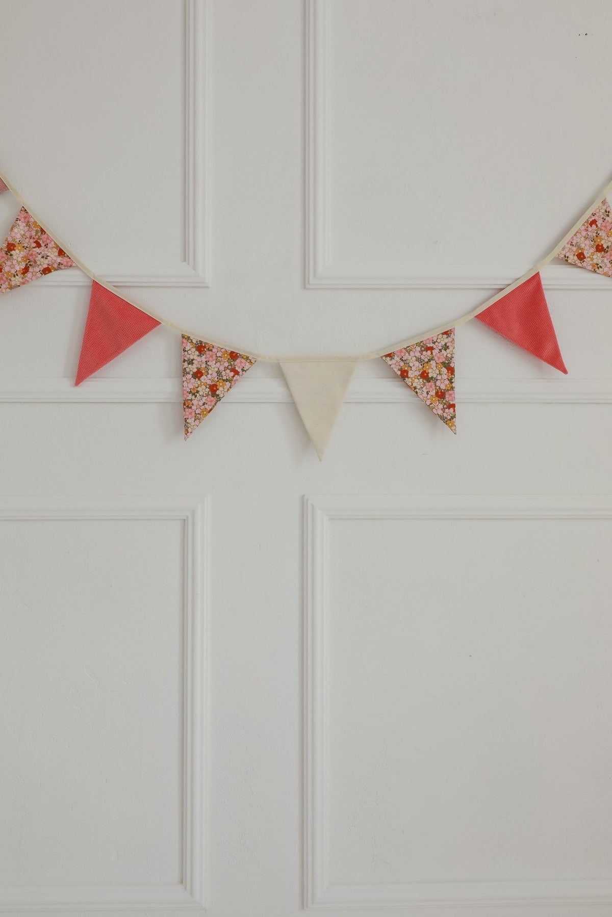 6. Close-up of garland with pink, floral, and beige pendants on a white paneled wall