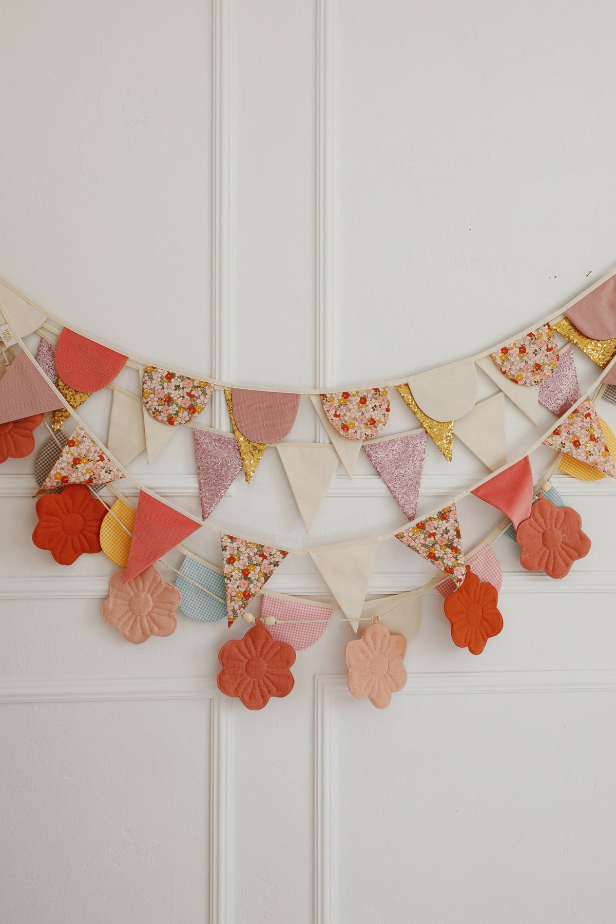 8. Layered garlands with pink, floral, and beige pendants and flower shapes on a white wall