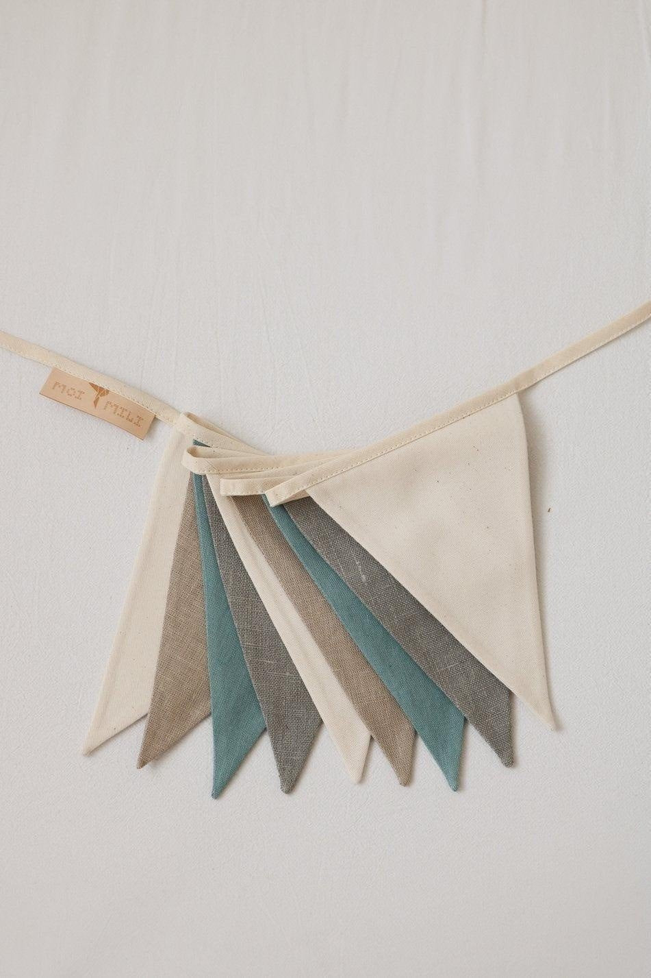 3. Detail of cream, grey, and teal linen pennants with moi mili label on light fabric background