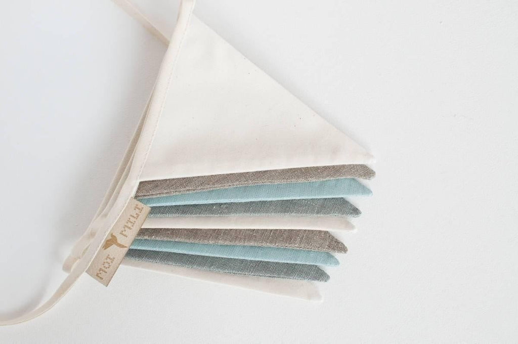 3. Close-up of cream, grey, and teal linen pennants stacked with moi mili label on white background