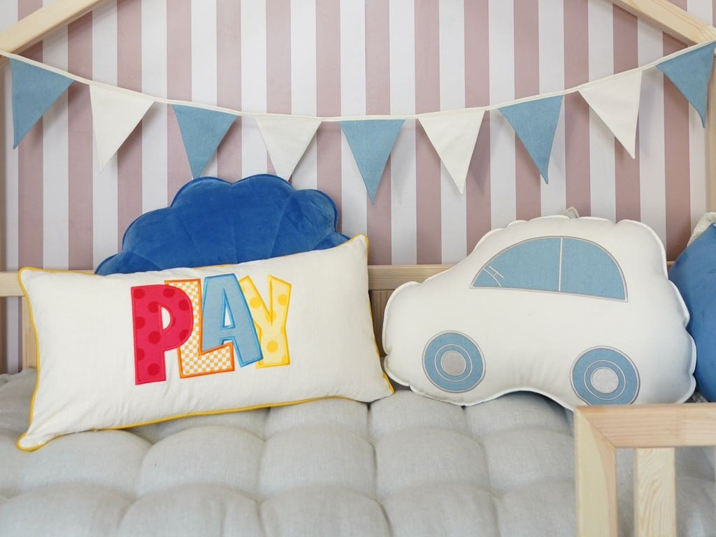 13. Close-up of play-themed cushion and blue and white garland on a child's bed