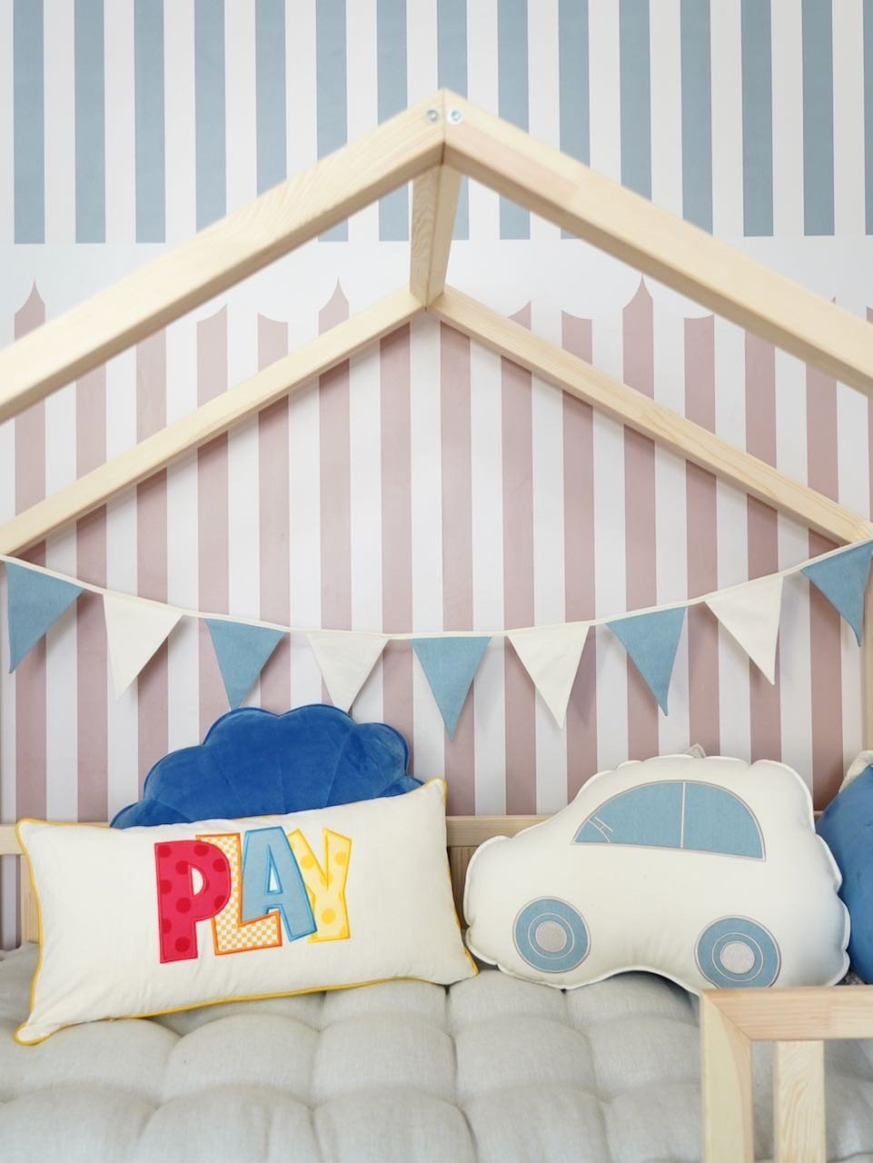 2. Children's bed with striped wallpaper, blue and white garland, and colorful play-themed cushions