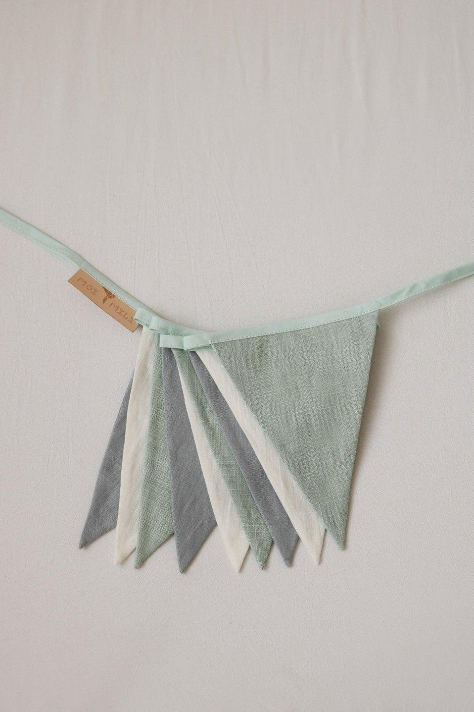 3. Close-up of mint, white, and grey cotton pennants on a garland with moi mili label on a light background