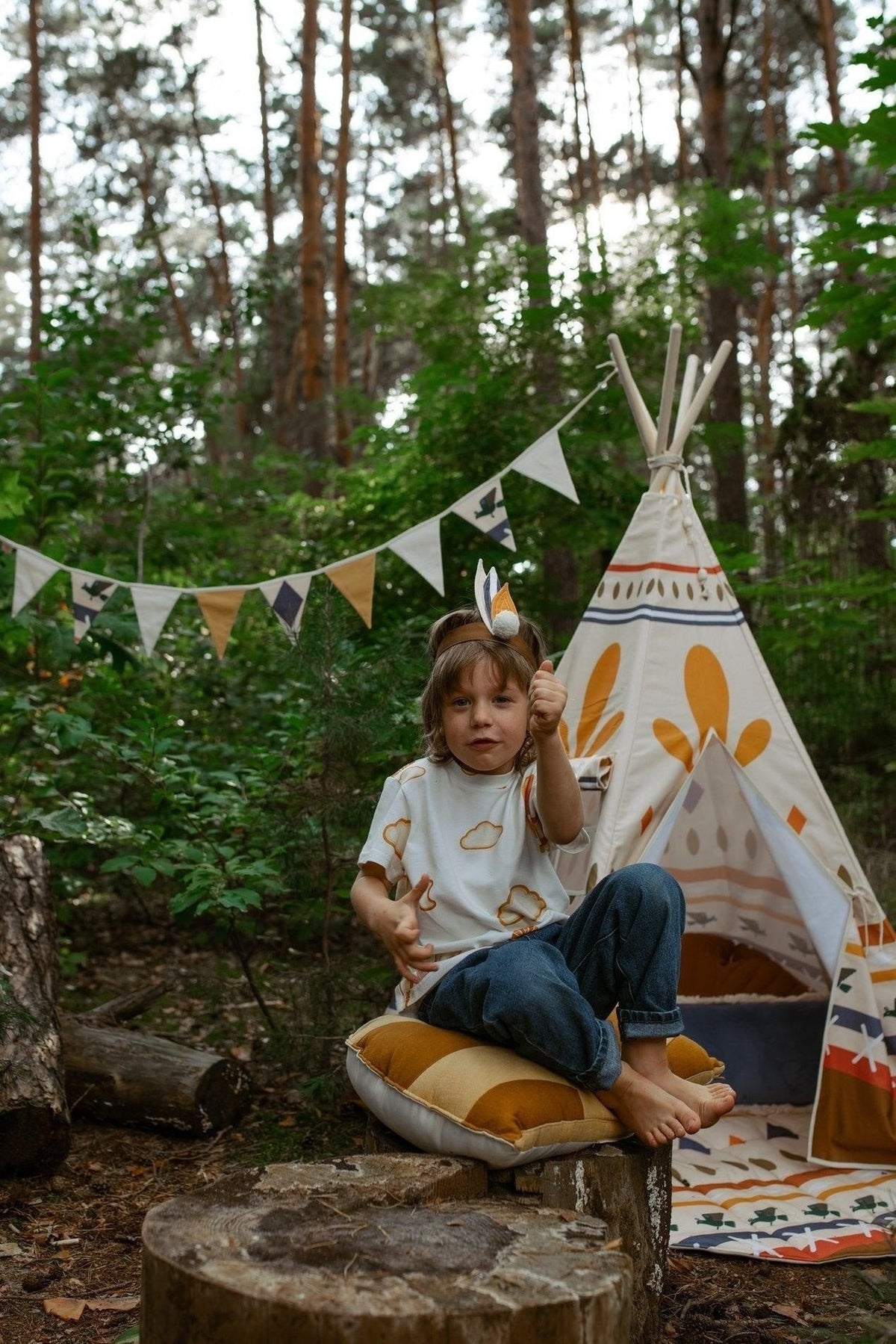 3. Child sitting on cushion in forest with teepee and Moi Mili Native Vibe garland in background