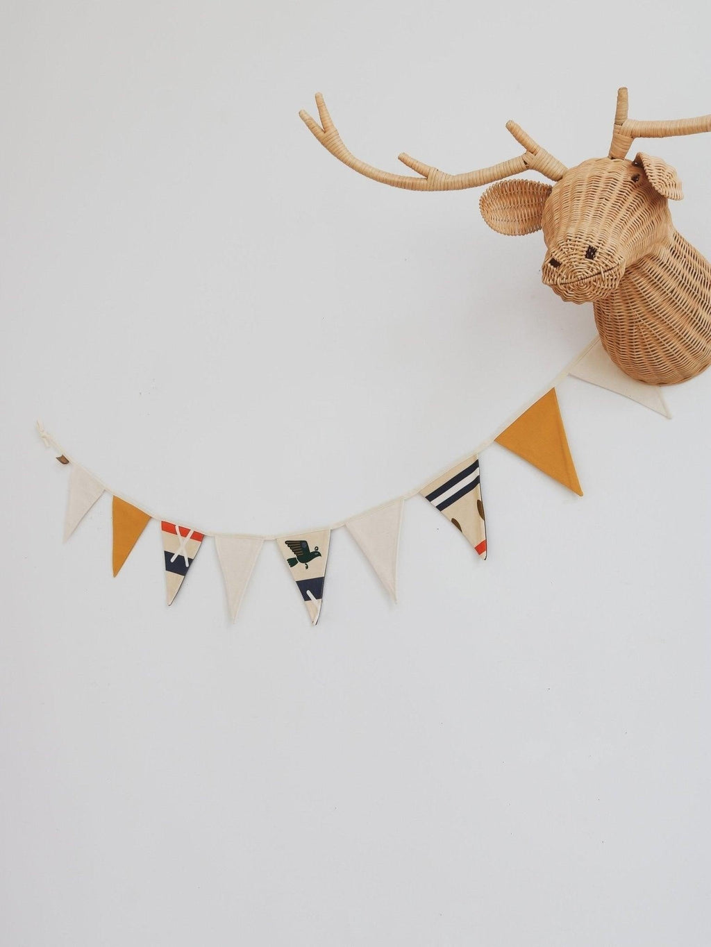 1. Cotton garland with geometric print and mustard yellow pennants hanging on white wall next to wicker deer head