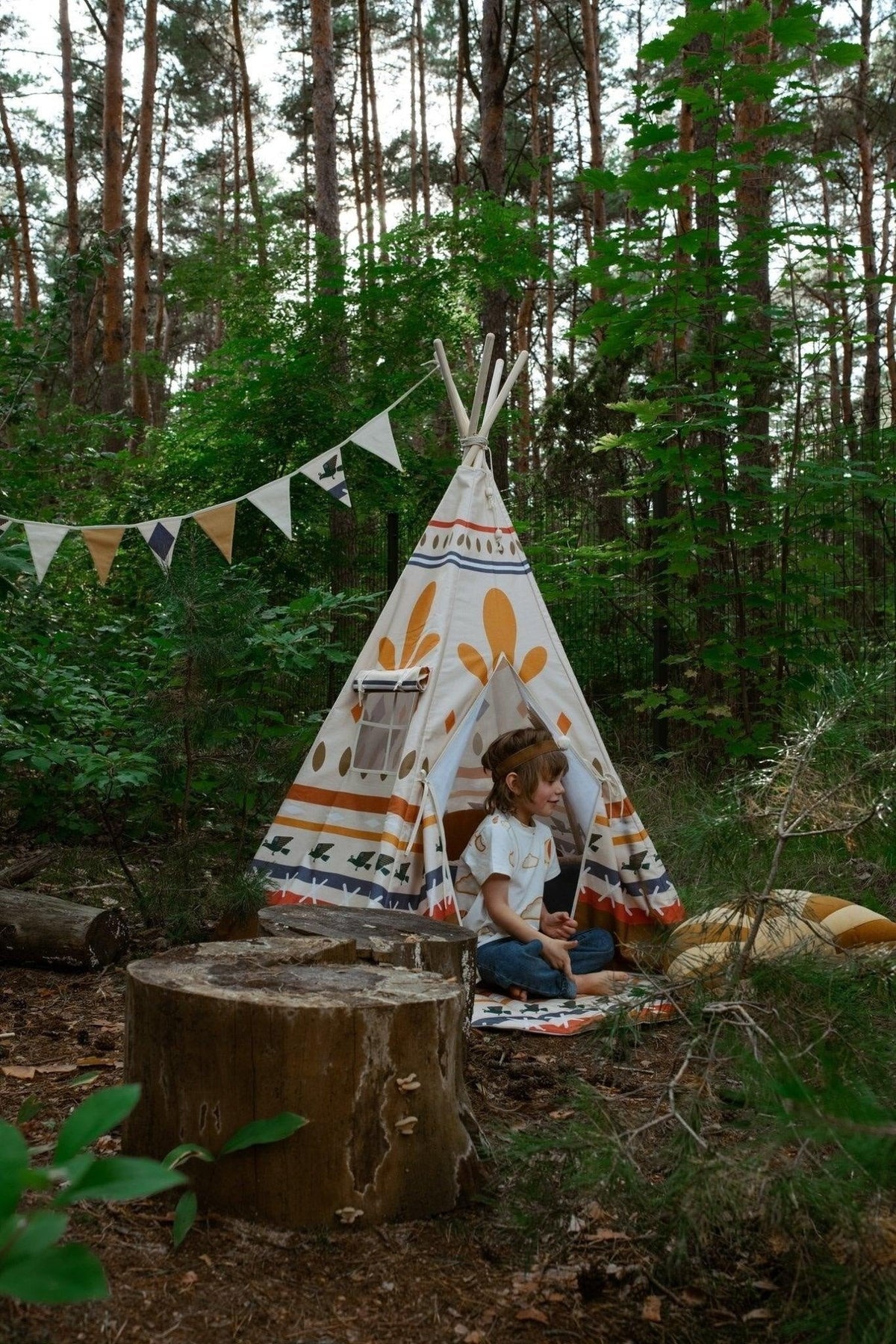 2. Two children sitting in forest with teepee and Moi Mili Native Vibe garland hanging between trees