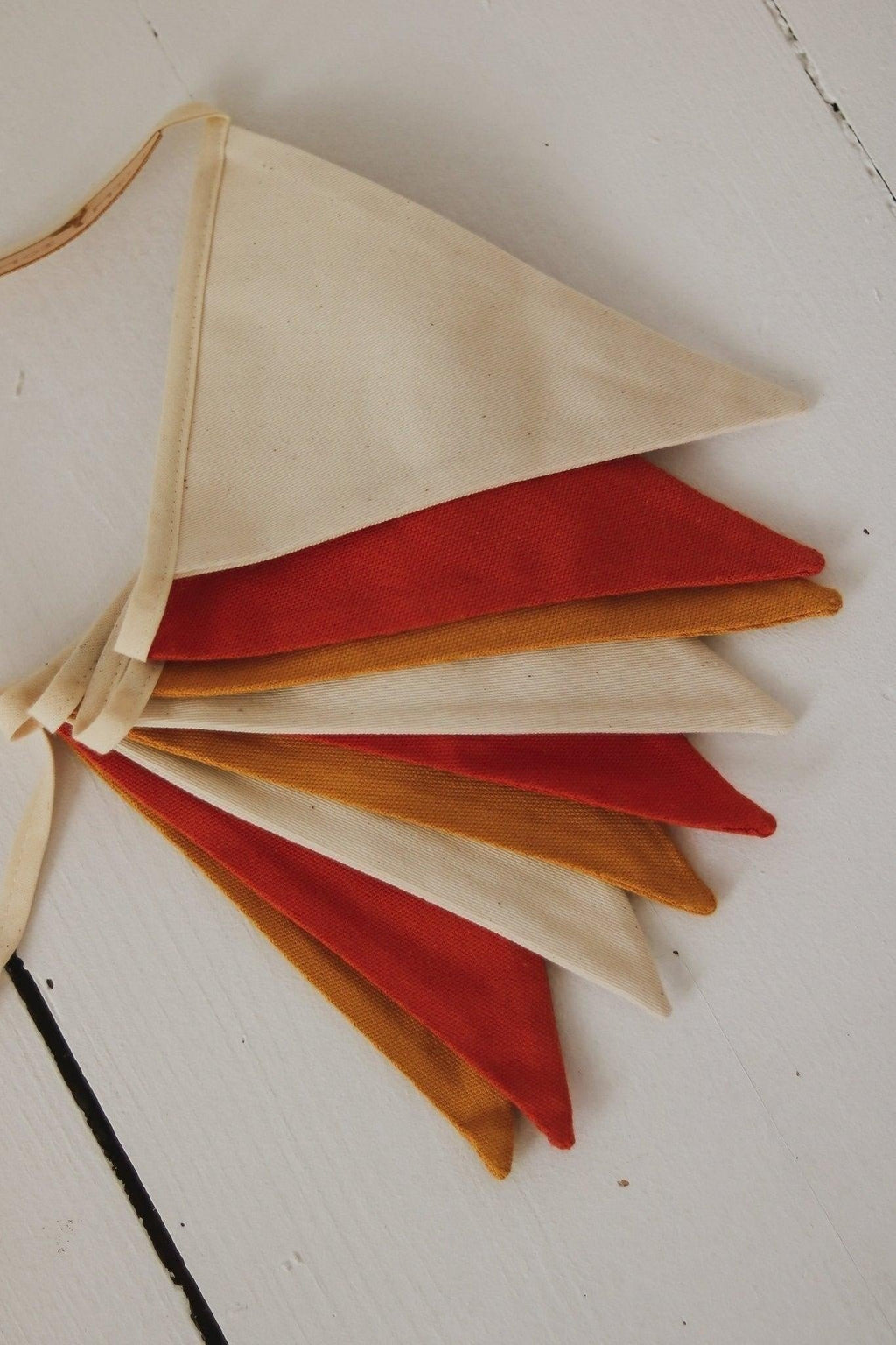 4. Flat lay of folded ochre garland with white, honey, and red pennants on a wooden surface