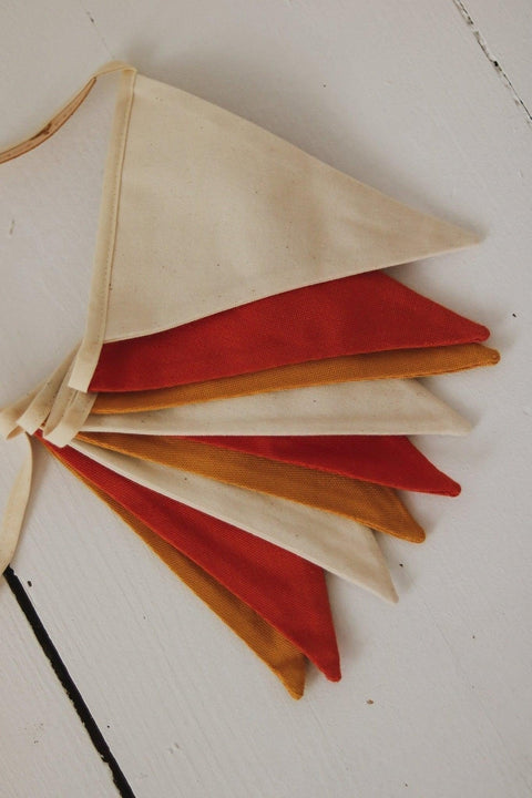 4. Flat lay of folded ochre garland with white, honey, and red pennants on a wooden surface