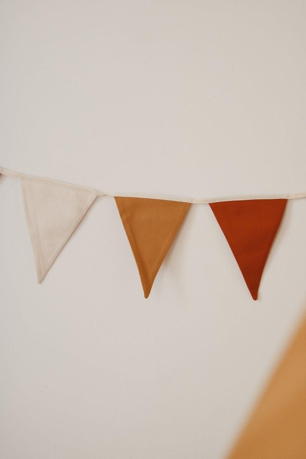 3. Close-up of ochre garland with white, honey, and red pennants against a light wall