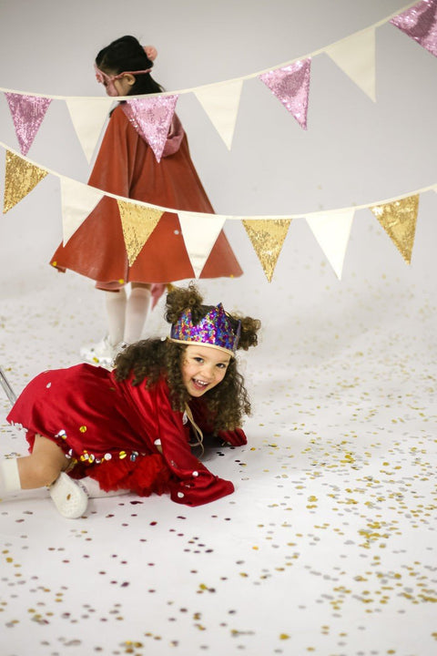 1. Two children playing with gold and beige sequin garland in festive setting with confetti