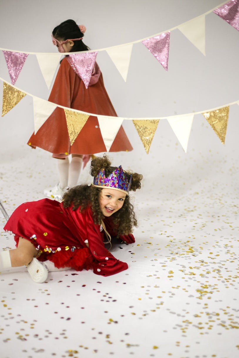 1. Two children playing under pink and beige sequin garland in a festive setting with confetti on the floor