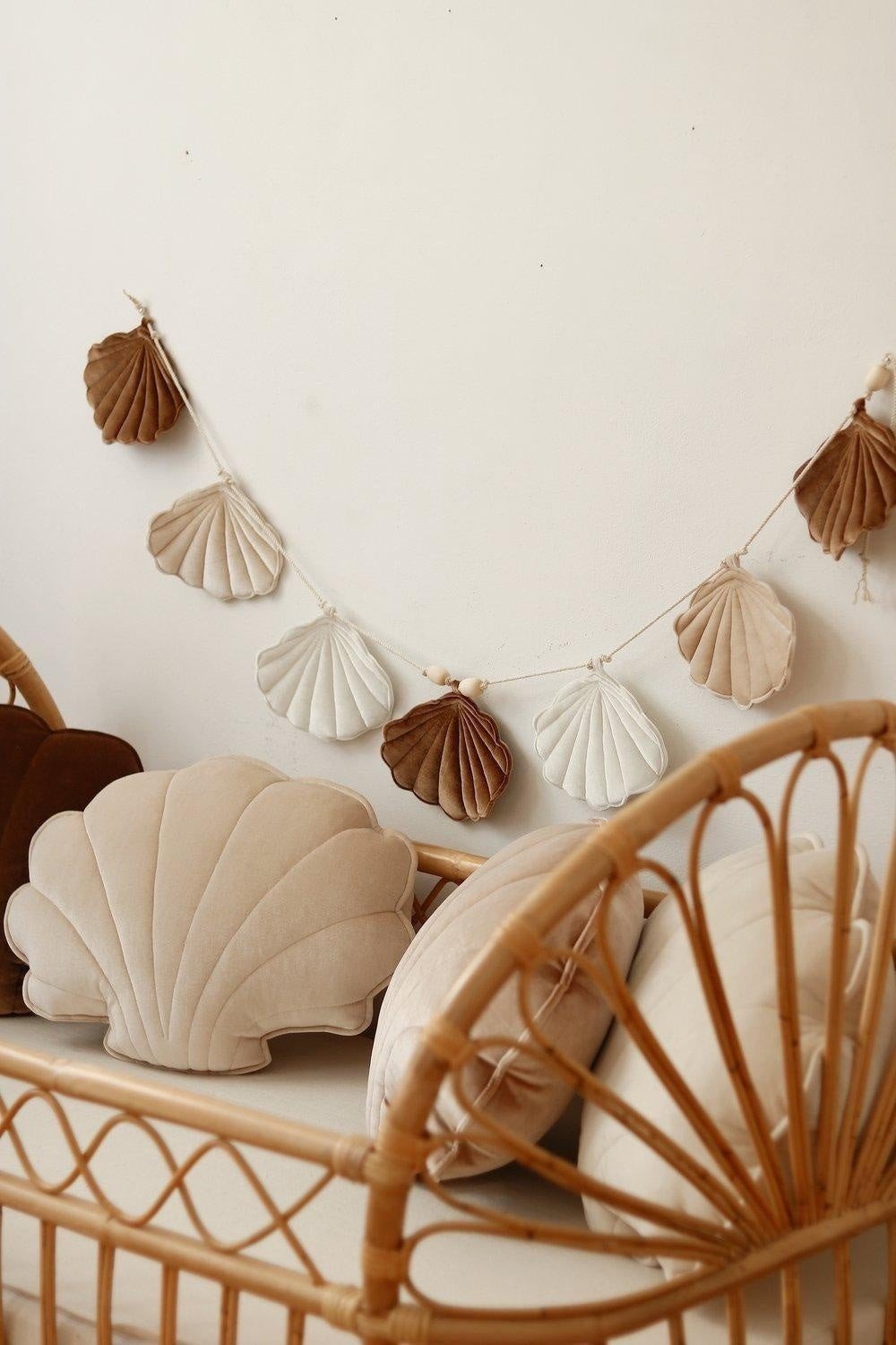 1. Beige and brown shell garland hanging above a rattan crib with shell-shaped cushions in a cozy room setting