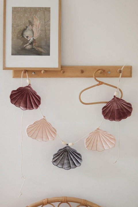 1. Velvet shell garland with marsala, pastel apricot, and grey shells hanging on a wooden hook in a child's room