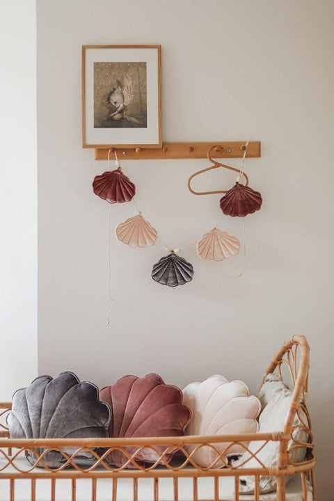 2. Velvet shell garland in marsala, pastel apricot, and grey above a wicker crib with matching shell cushions