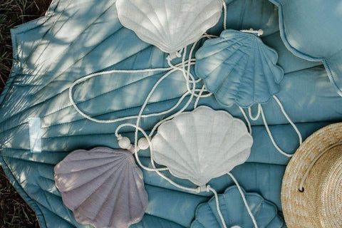 4. Close-up of shell garland with linen pendants in sky blue, grey, and desert sand on a blue quilt with a straw hat outdoors