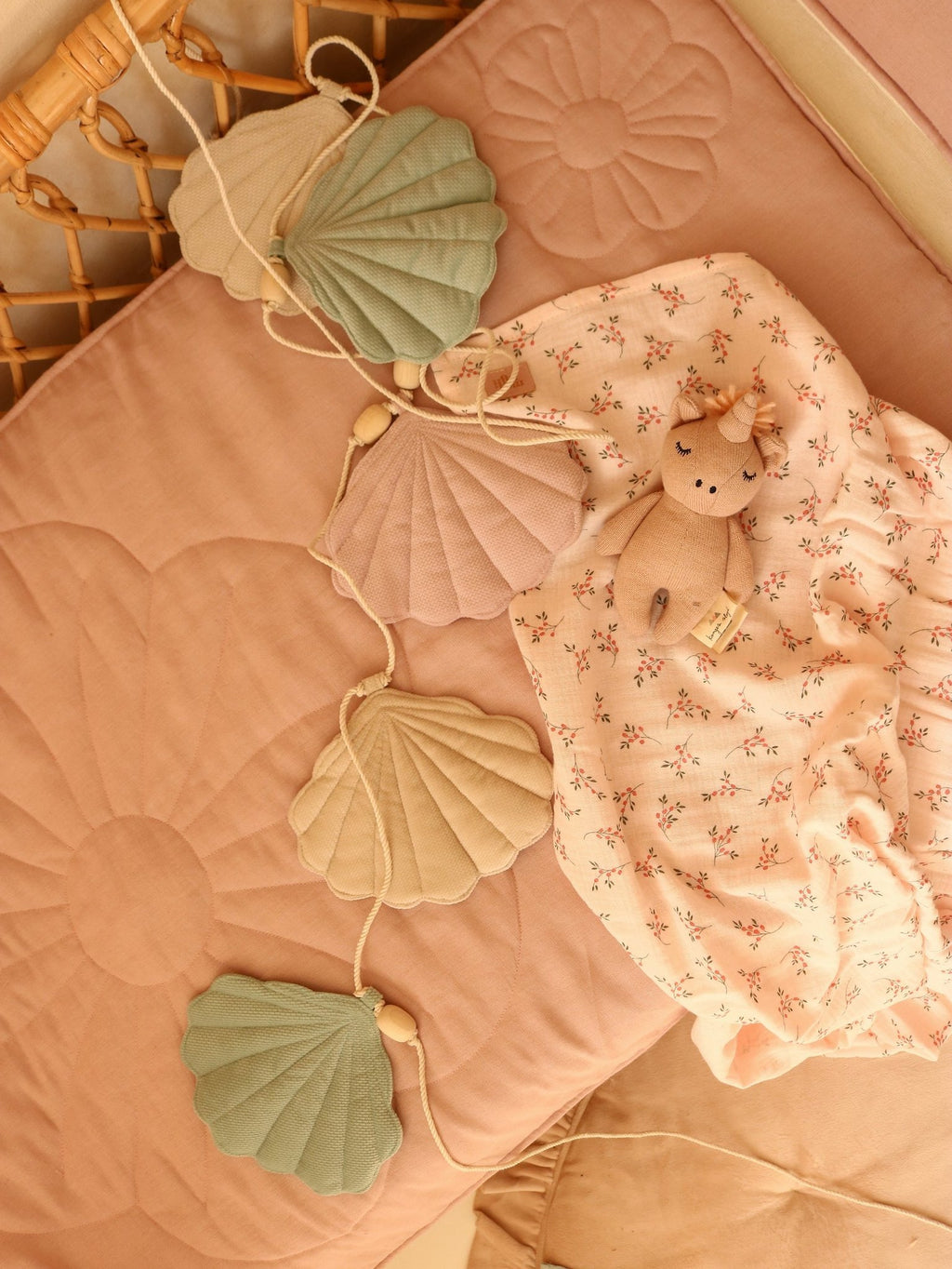 4. Flat lay of pastel shell garland on a pink quilted mat with a plush toy and floral blanket