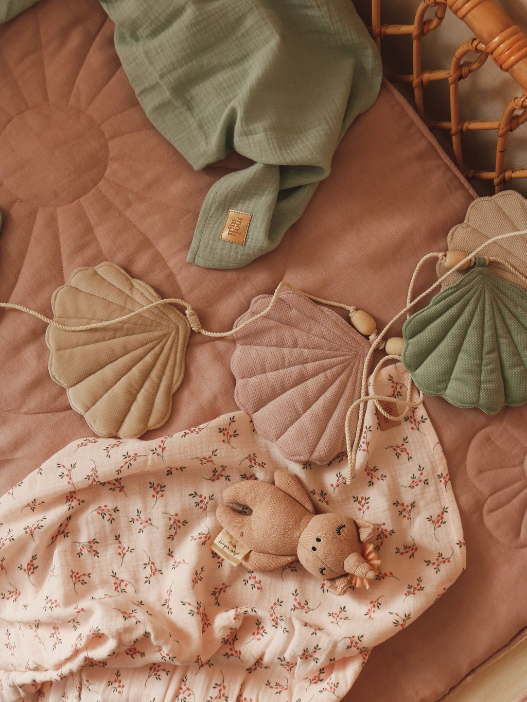 5. Pastel shell garland on a pink quilted mat with a plush toy and green blanket