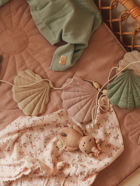 5. Pastel shell garland on a pink quilted mat with a plush toy and green blanket