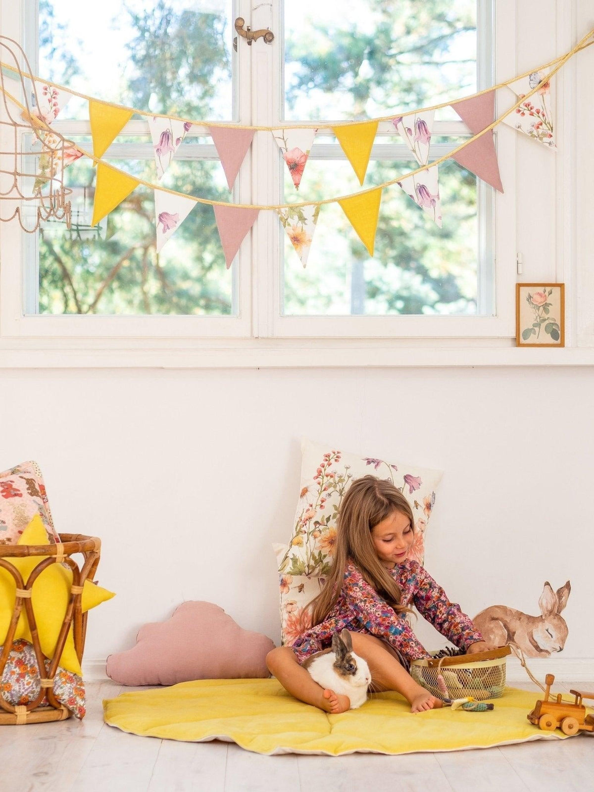 1. Child playing with toys in a room decorated with a floral and solid color garland hanging above, featuring yellow and pink pendants