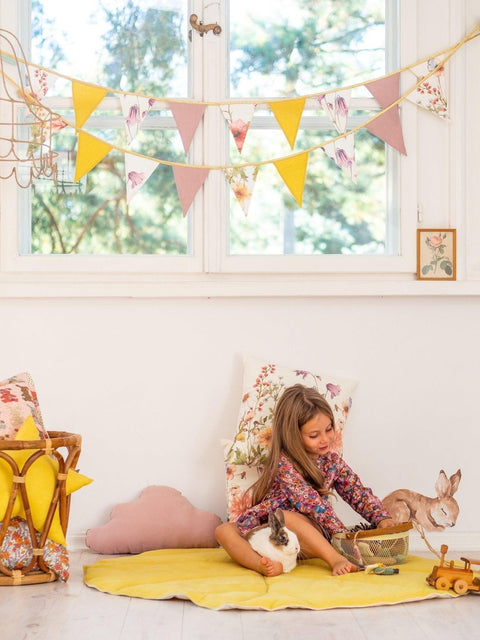1. Child playing with toys in a room decorated with a floral and solid color garland hanging above, featuring yellow and pink pendants