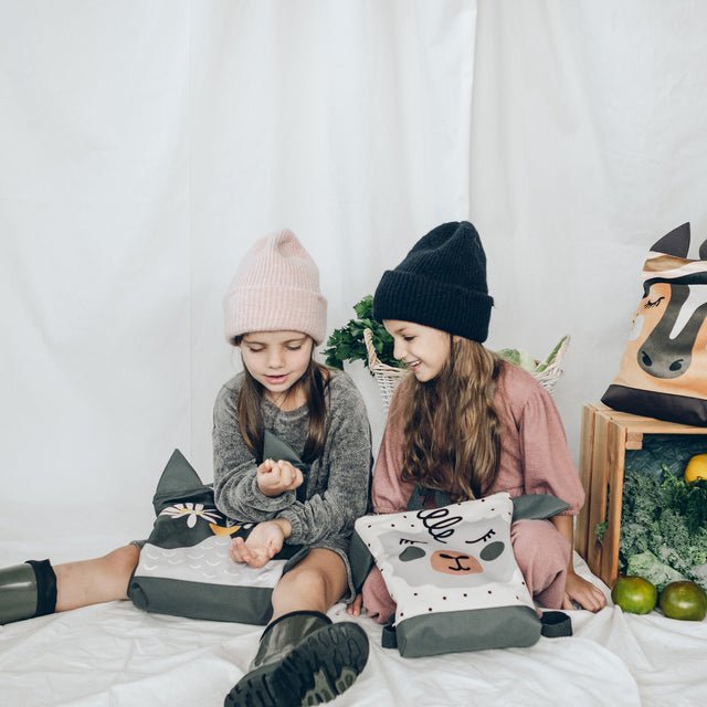 6. Two girls with Muni sheep backpacks, sitting and playing, showcasing the backpack's playful design