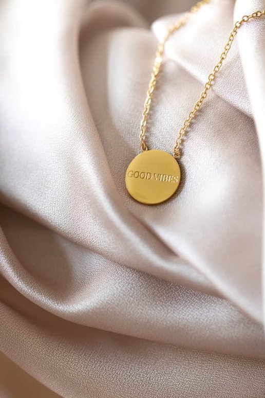 2. Close-up of Olla's Good Vibes necklace in gold on soft fabric, highlighting medallion detail
