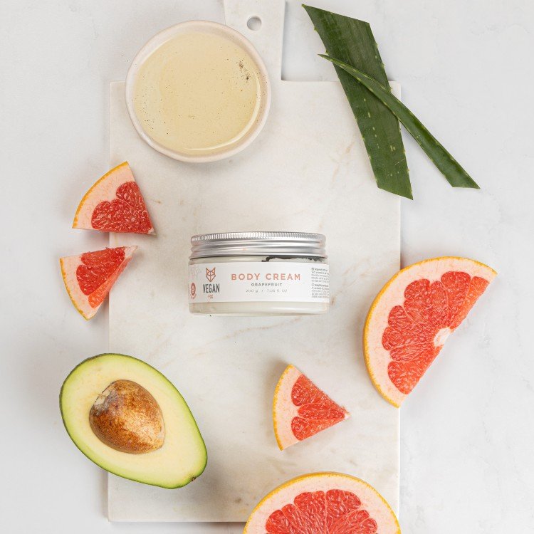 3. Vegan Fox Grapefruit Body Cream jar surrounded by grapefruit slices, avocado, and aloe vera on a marble surface