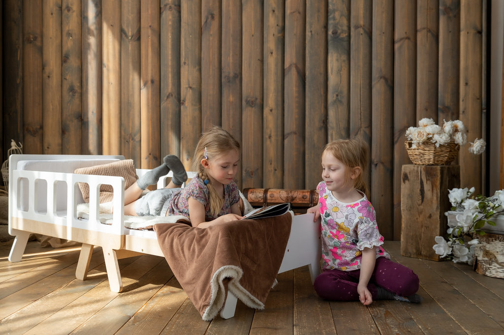11. Two children playing near white growing bed with brown blanket in wooden room
