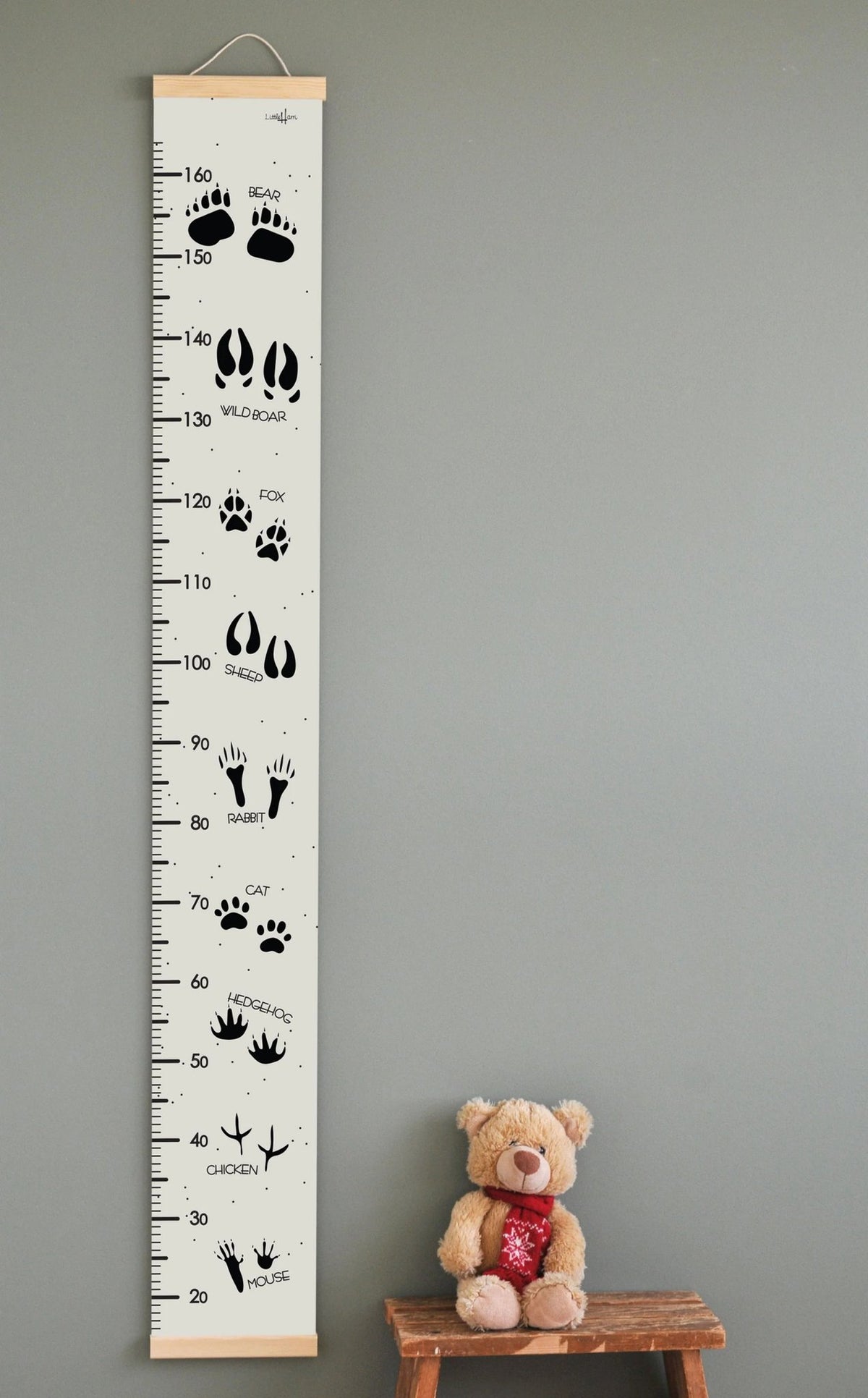 1. Kids' growth chart featuring animal tracks and names in English, printed on durable PVC fabric with wooden slats, hanging on a wall next to a teddy bear on a stool, ideal for playful home decor.