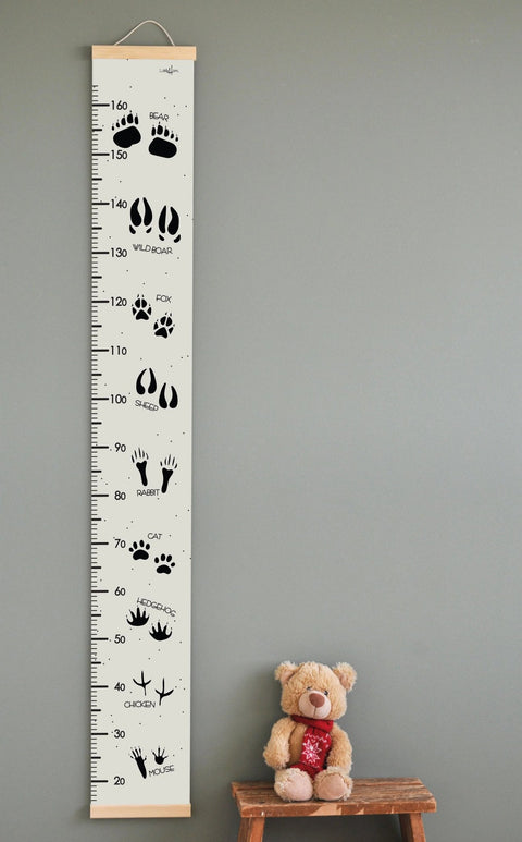 1. Kids' growth chart featuring animal tracks and names in English, printed on durable PVC fabric with wooden slats, hanging on a wall next to a teddy bear on a stool, ideal for playful home decor.