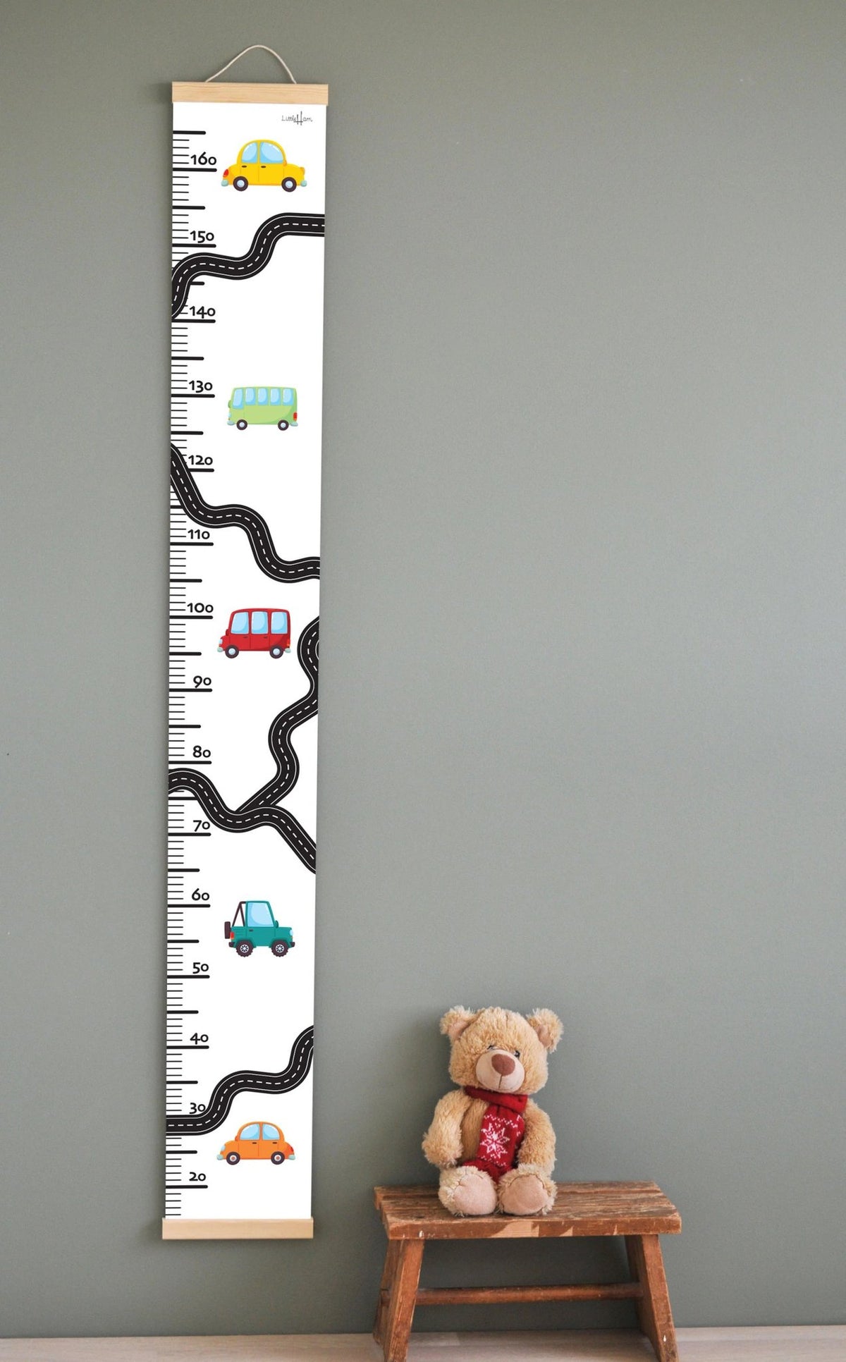 1. Children's growth chart with colorful car illustrations on a wall, featuring a measurement scale up to 165 cm, wooden slats, and attached string for hanging, next to a teddy bear on a stool.