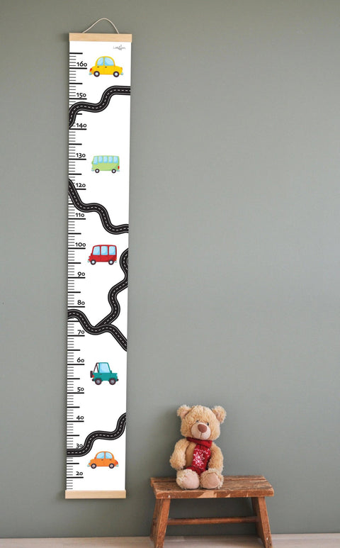 1. Children's growth chart with colorful car illustrations on a wall, featuring a measurement scale up to 165 cm, wooden slats, and attached string for hanging, next to a teddy bear on a stool.