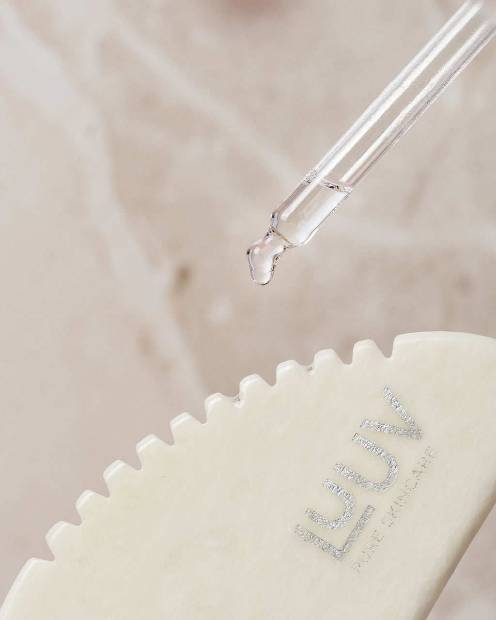 2. Close-up of LUUV Gua Sha for Body with toothed edge and dropper applying oil, highlighting jade texture and brand logo