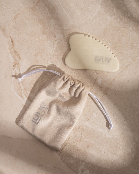 1. LUUV Gua Sha for Body made from natural white jade with toothed edge, shown on marble surface with branded drawstring pouch