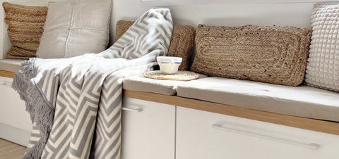 2. Labbvenn gray and white pet blanket with linear patterns on a bench surrounded by textured cushions and a cup on a woven coaster