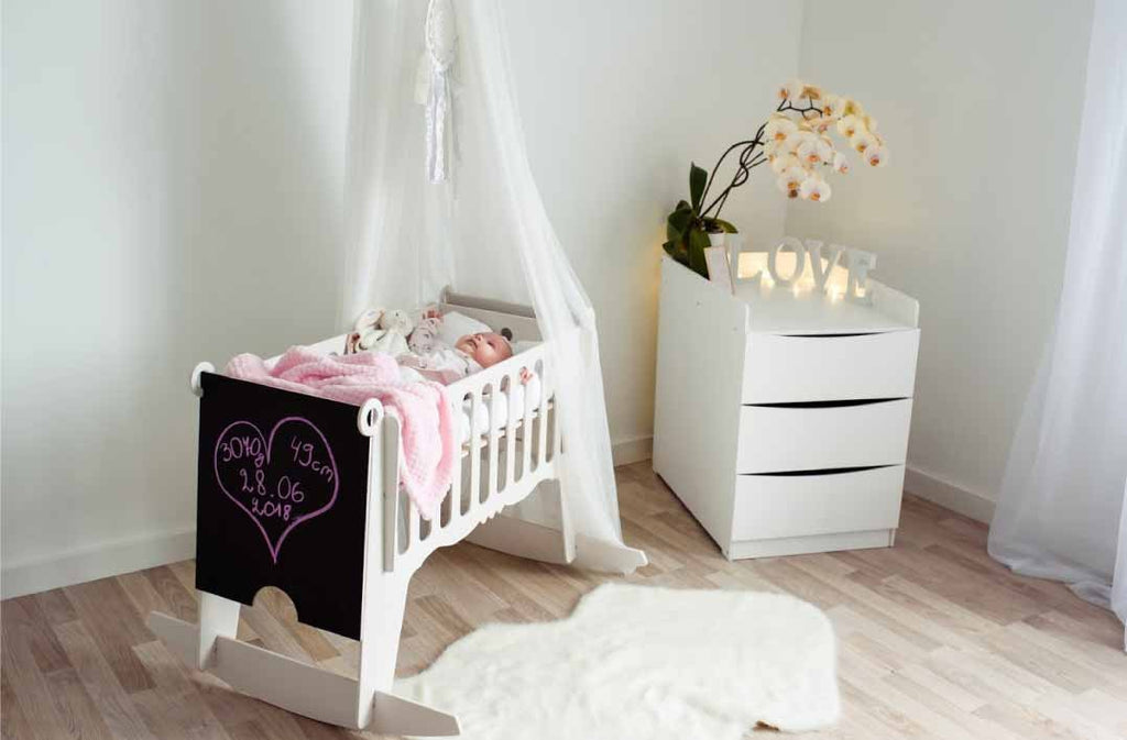 1. Baby sleeping in white Adensen birchwood cradle with pink blanket in cozy nursery setting