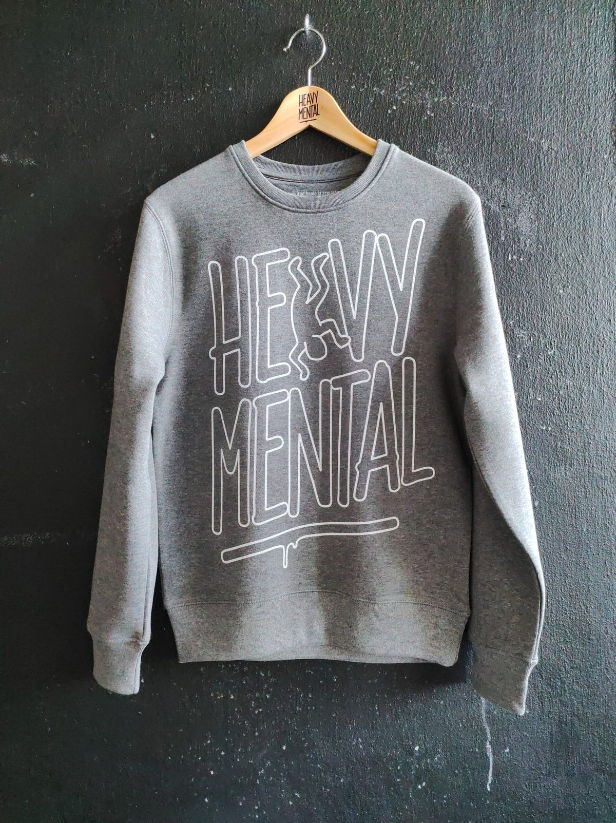1. Grey Heavy Mental sweatshirt with Keith Haring-inspired print, shown hanging against a dark wall