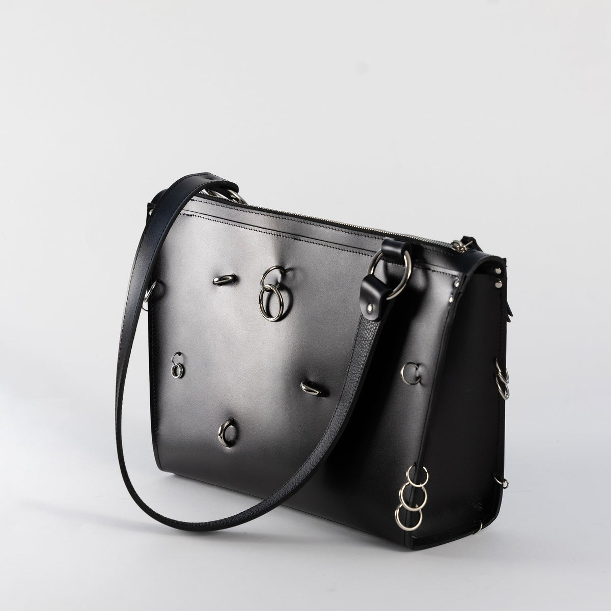 1. Black leather ARINA handbag with silver decorative rings and shoulder strap on white background