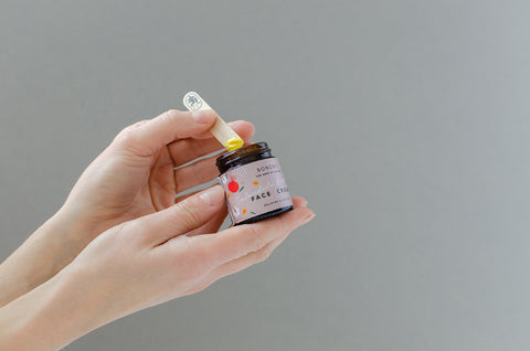 1. BONOBO Calendula & Rosehip Face Cream held by hands with juniper spatula, showcasing packaging and product