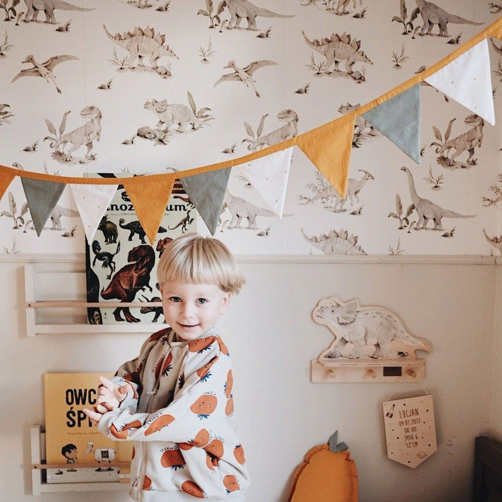 7. Smiling child in room with dinosaur wallpaper, colorful bunting, and wooden shelves
