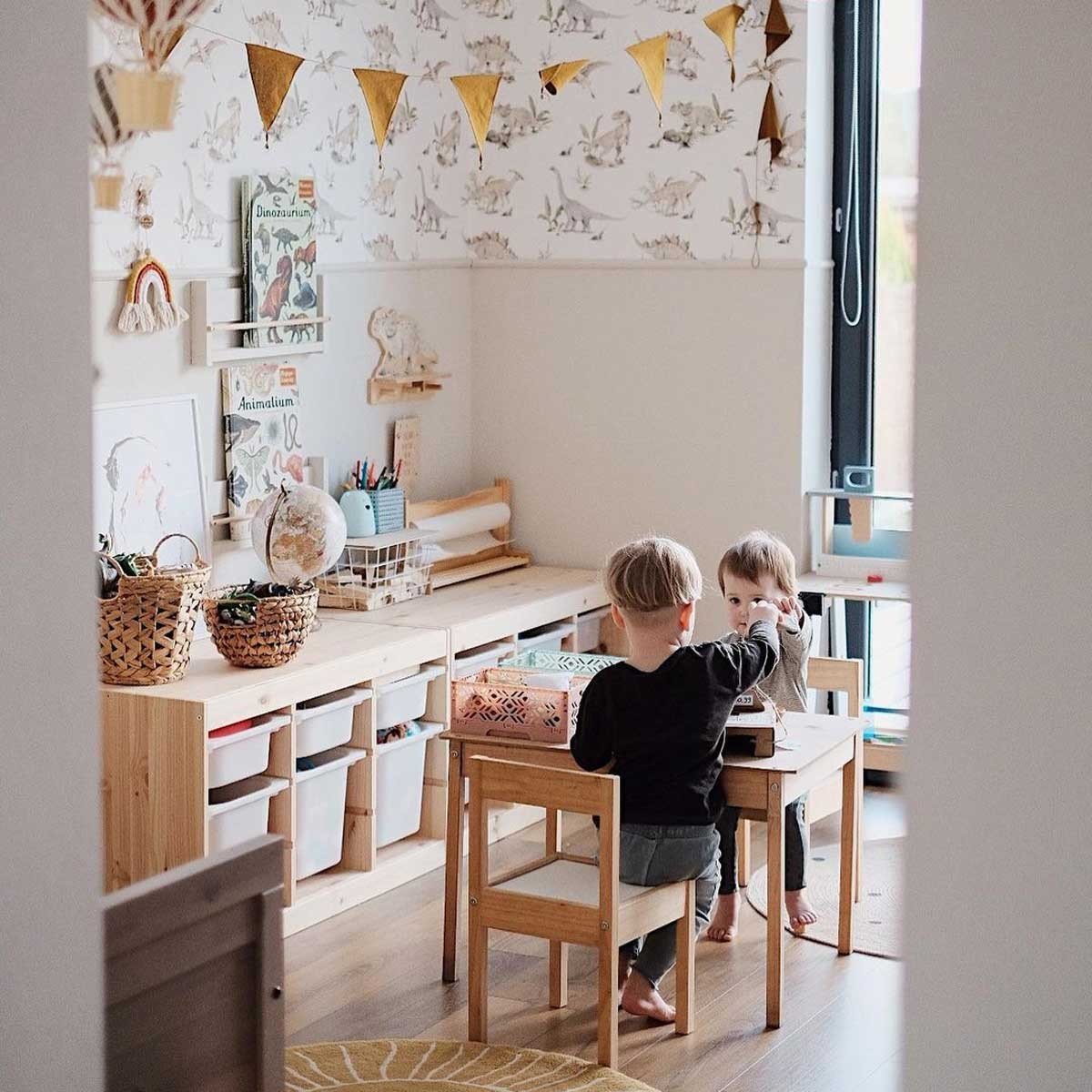 2. Two children playing in a room with dinosaur wallpaper, wooden furniture, and decorative bunting