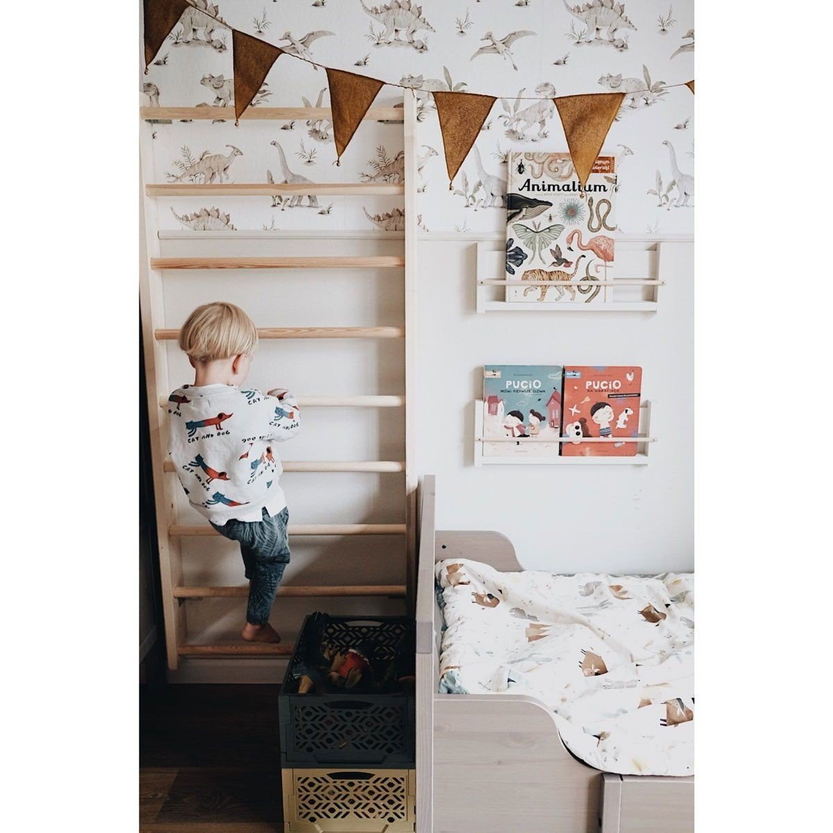 4. Child climbing wooden frame in room with dinosaur wallpaper and decorative bunting