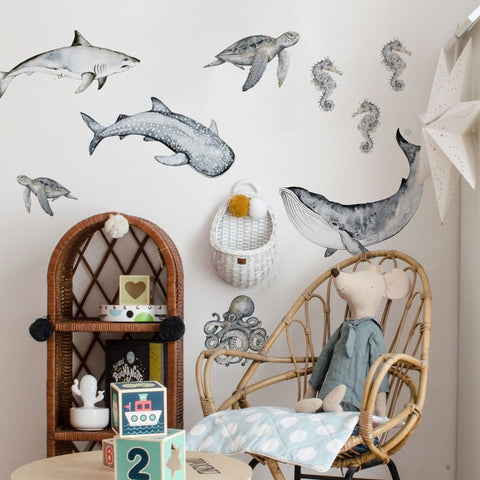 1. Children's room with Happy Ocean Wonderland wall stickers featuring a shark, whale shark, turtles, seahorses, octopus, and whale above a wicker chair and toys