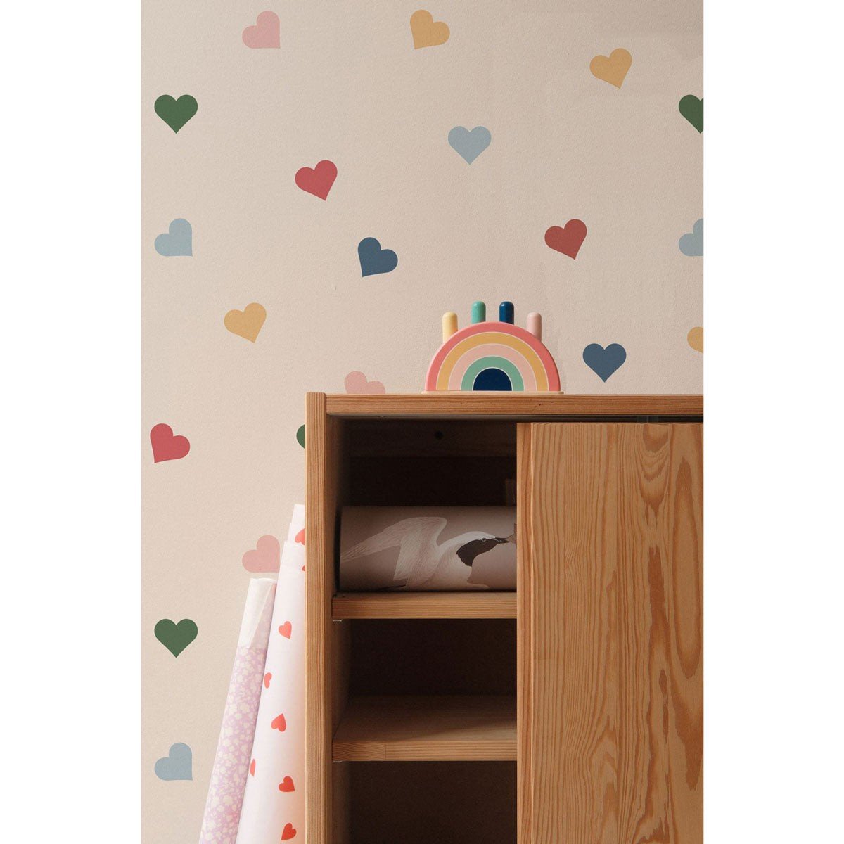 2. Close-up of colorful heart-patterned wallpaper by Dekornik behind a wooden cabinet with a rainbow toy on top